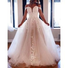 a woman in a white wedding dress standing on a wooden floor with her hands behind her back