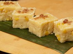 four pieces of cake sitting on top of a green leaf covered plate with yellow toppings