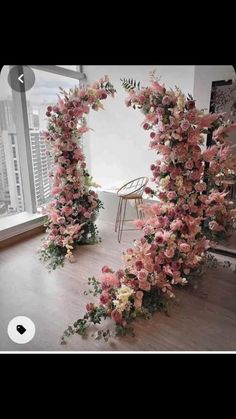 an arch made out of pink flowers in front of a large window with a chair