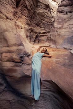 a woman standing in the middle of a canyon wearing a blue dress and holding her hands behind her head