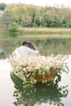 a bride and groom are sitting in a rowboat on the water with their arms around each other