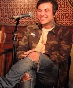 a young man sitting in front of a microphone and talking into a cell phone while smiling