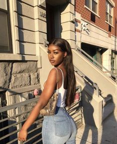 a woman standing on the sidewalk in front of a building wearing high waist jeans and a white tank top