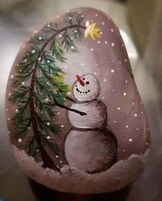 a painted rock with a snowman holding a pine tree