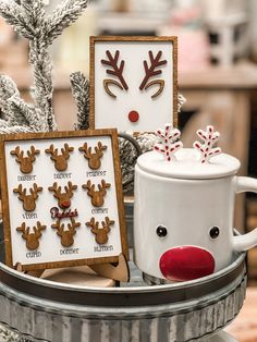 some christmas cookies are sitting in a tin with reindeer faces on them and one is holding a mug