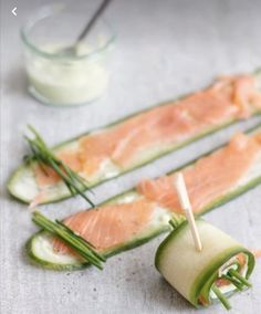 cucumber wrapped in green onions with toothpicks sticking out of them and sauce on the side