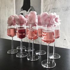 five wine glasses filled with pink liquid and cotton floss in front of a black table