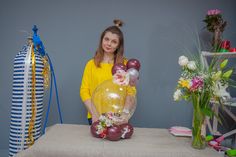 a woman standing next to a table with balloons and flowers in vases on it