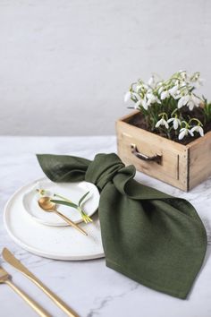 a white plate topped with a green bow tie next to a wooden box filled with flowers