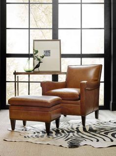 a chair and ottoman in front of a large window with zebra rug on the floor