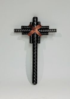 a black cross with a brown ribbon hanging from it's side on a white wall