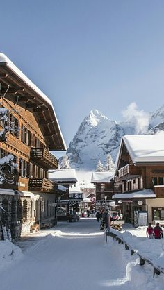 people are walking in the snow near some buildings and mountain tops with snow on them