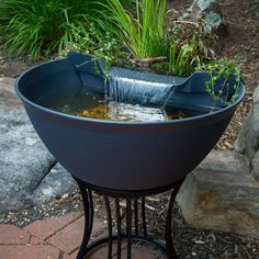 a planter filled with water sitting on top of a metal stand next to rocks