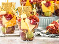 fruit and cheese appetizers in small cups on a table with crackers, olives, strawberries