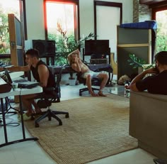 two men and a woman are sitting in an office with computer monitors on the wall