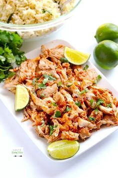 a white plate topped with chicken and rice next to limes, cilantro