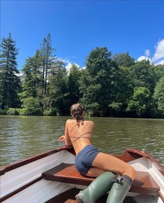 a woman is sitting on the back of a boat in the water with trees behind her