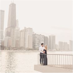 a man and woman standing next to each other near the water in front of tall buildings