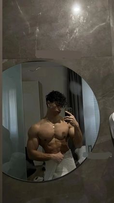 a shirtless man taking a selfie in front of a mirror with his cell phone