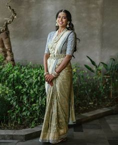 a woman in a white and gold sari posing for the camera with her hands on her hips