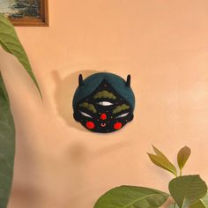 a black mask with red eyes is hanging on the wall next to a potted plant