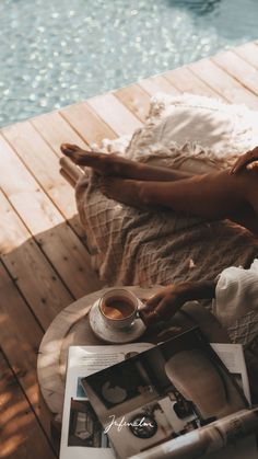 a woman laying on a wooden deck next to a pool with a cup of coffee