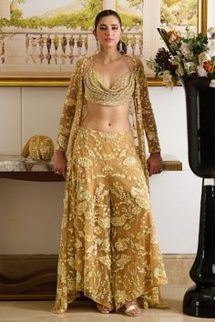 Gold full sleeves longline cape with all over marigold bloom embroidery using tonal sequin, beads, pearls, crystals highlights. Paired with scallop embroidered sweetheart cowl neck blouse and garden embroidered flared pant. - Aza Fashions Fitted Gold Embroidery Palazzo Set, Long Sleeve Gold Choli For Festive Occasions, Gold Long Sleeve Palazzo Set For Festive Occasions, Fitted Palazzo Set With Gold Embroidery For Wedding, Gold Embroidered Long Sleeve Sets For Receptions, Gold Embroidery Long Sleeve Sets For Reception, Long Sleeve Sets With Gold Embroidery For Reception, Fitted Gold Palazzo Set With Intricate Embroidery, Festive Gold Palazzo Set With Long Sleeves