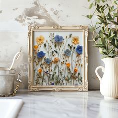 an ornate gold frame with blue and yellow flowers on it next to a potted plant