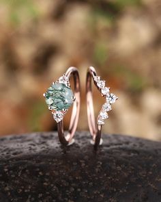 two wedding rings with green and white stones on top of each other, sitting on a rock