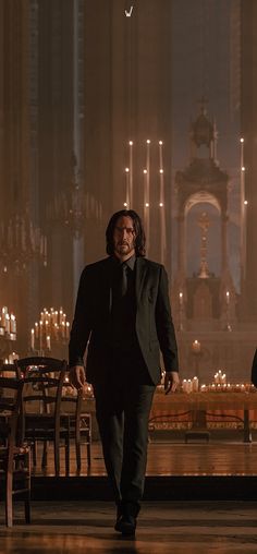 a man in a suit and tie walking through a room with candles on the walls