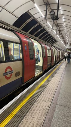 a subway train pulling into the station with people walking on the platform next to it