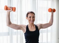 a woman holding two dumbs in front of her face and smiling at the camera