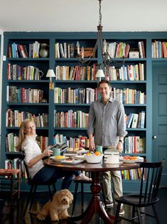 two people sitting at a table in front of bookshelves with a dog on the floor