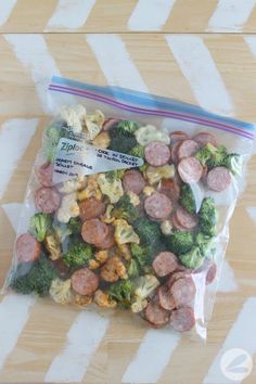 a bag filled with sausage and broccoli sitting on top of a wooden table