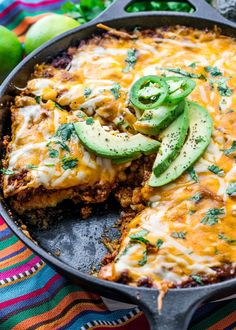 an enchilada casserole in a cast iron skillet with sliced avocado on top