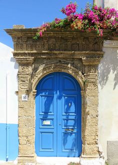 a blue door with flowers on the ledge above it and an arched doorway to another building