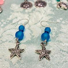 These Pierced Earrings Have Beautiful Blue Sea Glass Beads Separated With Swarovski Blue Bicones. The Starfish Dangle Is Medal And Etched Design On One Side. A Wonderful Gift! Handmade Silver Starfish Earrings, Blue Star Charm Drop Earrings, Blue Drop Earrings With Star Charm, Silver Ocean-inspired Earrings With Starfish Charm, Silver Drop Earrings With Starfish Charm, Ocean-inspired Silver Earrings With Starfish Charm, Blue Starfish Charm Earrings For Gift, Ocean-inspired Blue Jewelry With Star Charm, Silver Starfish Shaped Beaded Jewelry