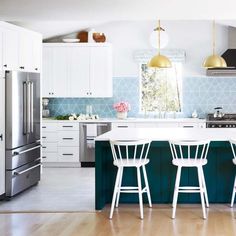 a kitchen with blue and white tile backsplash, gold pendant lights over the island