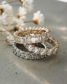 three wedding rings sitting next to each other on top of a table with flowers in the background