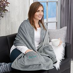 a woman sitting on a couch holding a cup and blanket