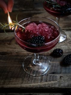 a person lighting a candle on top of a wine glass filled with berries and ice