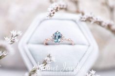 an engagement ring with a blue topazte surrounded by white flowers and branches in front of a velvet jewelry box