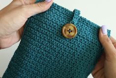 a person holding a green crocheted pouch with a button on it and two hands