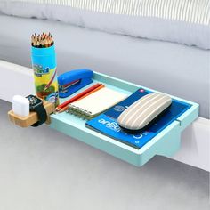 a blue tray with pencils, pens and other items on it next to a white bed