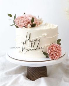 a white cake with pink flowers on top and happy birthday written on the side next to it