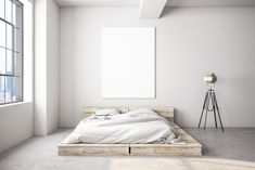 an empty bed with white sheets and pillows in a room next to a large window