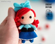 a crocheted doll is held in the palm of someone's hand with red hair and blue dress