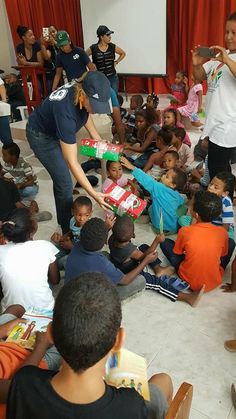 a group of children sitting on the floor in front of a woman holding a cake