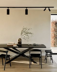 a dining room table with chairs and a vase on top of it, in front of an open window