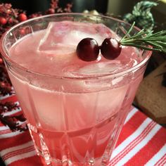 two cherries sit on top of a drink in a glass with ice and rosemary